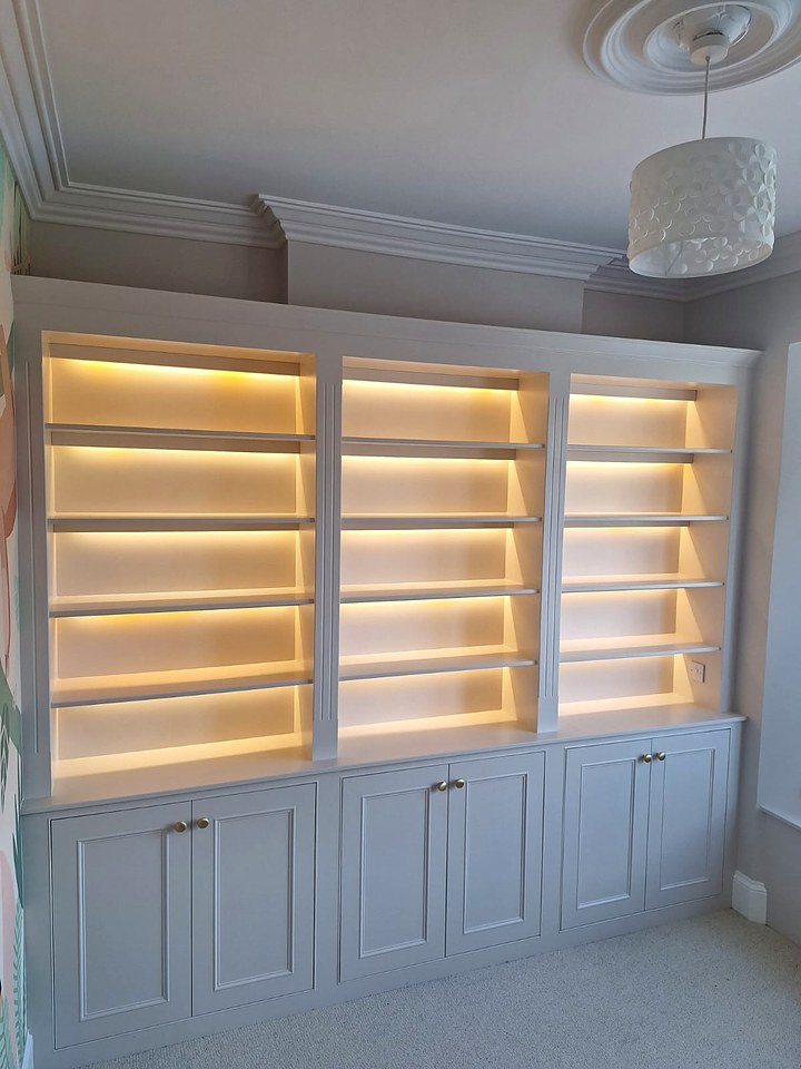 Fitted white bookcase with warm LED strip lighting under every shelf