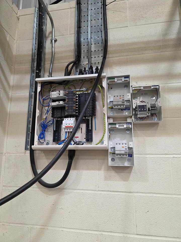 Commercial distribution board with sub-main cables in steel trunking and cable tray, beside separate isolator and control enclosures on a block wall