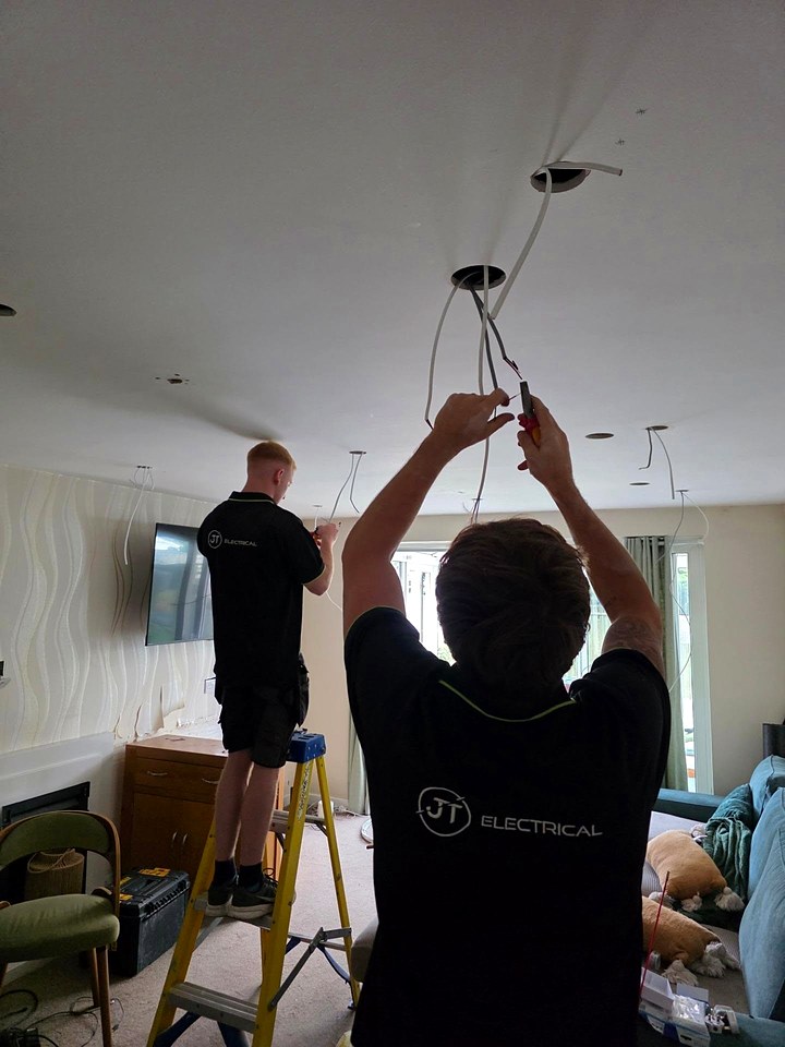 Two JT Electrical electricians, seen from behind, wiring new ceiling downlights in a living room