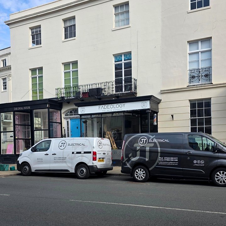 Two JT Electrical vans, one white and one dark grey, parked outside shops on a Georgian street in Leamington Spa